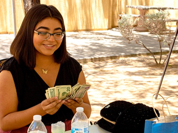 A young woman counts cash and smiles after participating in a NAYEP market event in 2019.