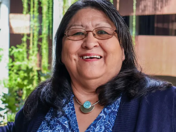 Joan Timeche smiles in a blue blouse, navy cardigan and turquoise necklace at U of A's ENR2 building.