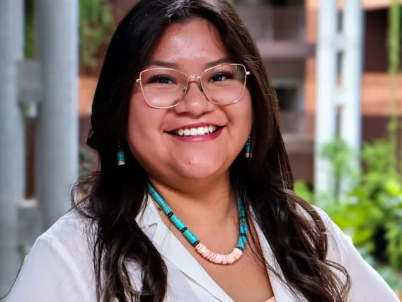 Kyra James smiles in a white blouse and turquoise bead necklace at U of A's ENR2 building.