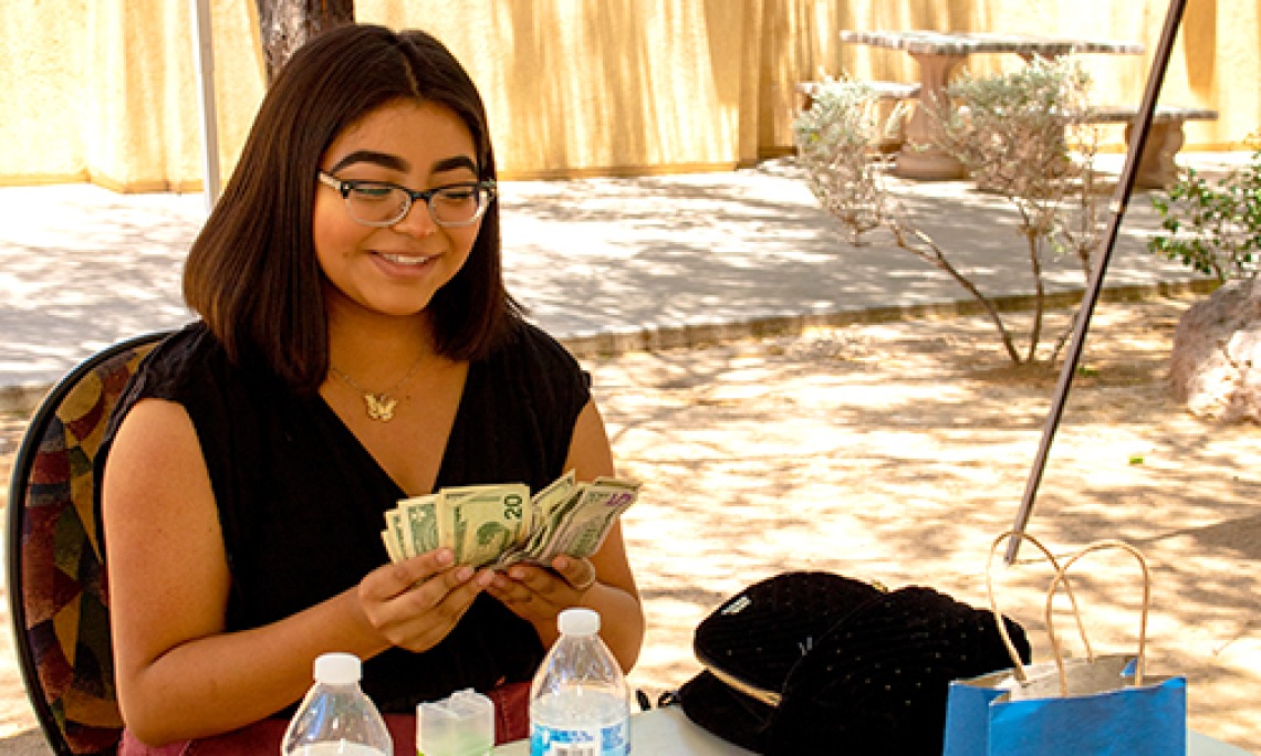 A young woman counts cash and smiles after participating in a NAYEP market event in 2019.
