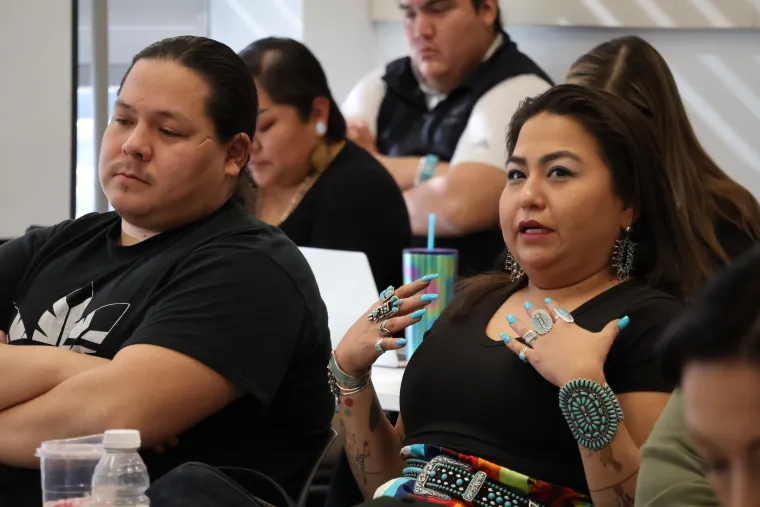 A young woman in an elaborate set of turquoise jewelry and black tank top speaks to the group during a JIT course.