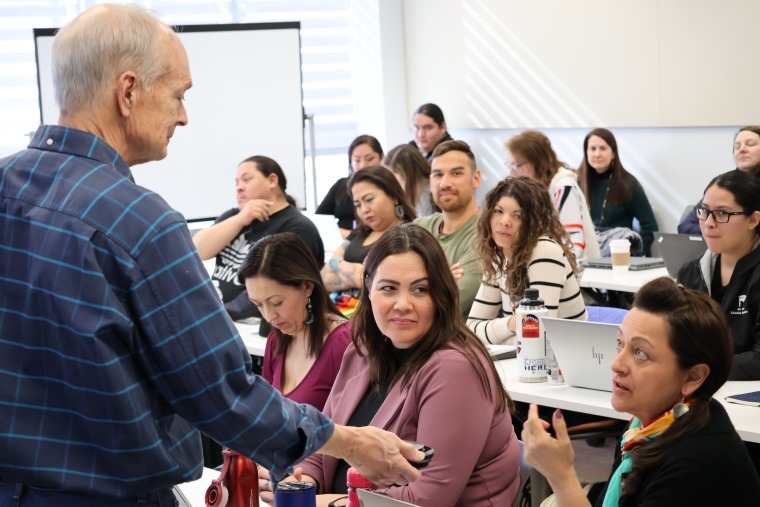 Steve Cornell in a dark blue plaid shirt holds a digital microphone to a student who is speaking during his Intro to Native Nation Building course.