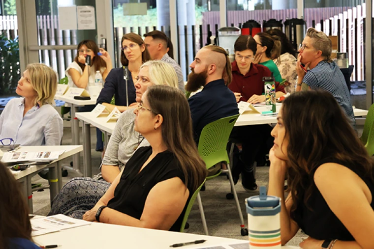 Attendees look on from a series of tables as Native Know How content is delivered by an instructor from outside the fram