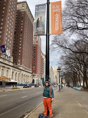 Mary Beth Jager points upward while standing under an AGU banner in Chicago.
