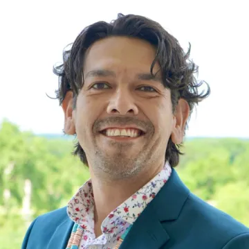 A portrait of Justin Lund outdoors in a blue jacket and floral collared shirt.