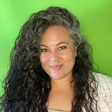 Bianca Villaseñor wears a white blazer with thin black lines arranged in a grid as she stands in front of a green screen.