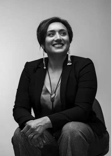 Black and white photo of Producer Maggie Cunningham in a dark suit against a gray background.