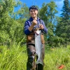 Torin Jacobs II poses in waders with a large fish, likely a Chinook salmon, on a sunny day in Alaska.