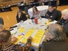 Session attendees sit around a round table with a white table cloth as they work to fill in yellow note cards to present to the larger group.
