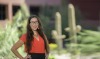Stephanie Russo Carroll poses in front of saguaro cacti in a red shirt.