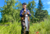 Torin Jacobs II poses in waders with a large fish, likely a Chinook salmon, on a sunny day in Alaska.
